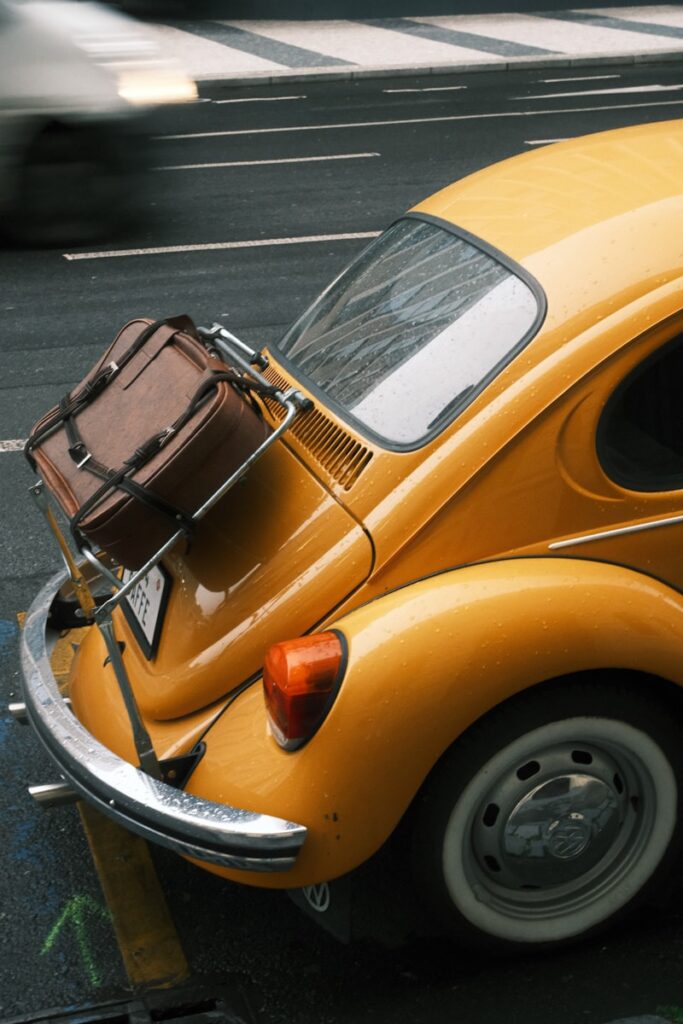 Yellow vintage car with luggage on the trunk.